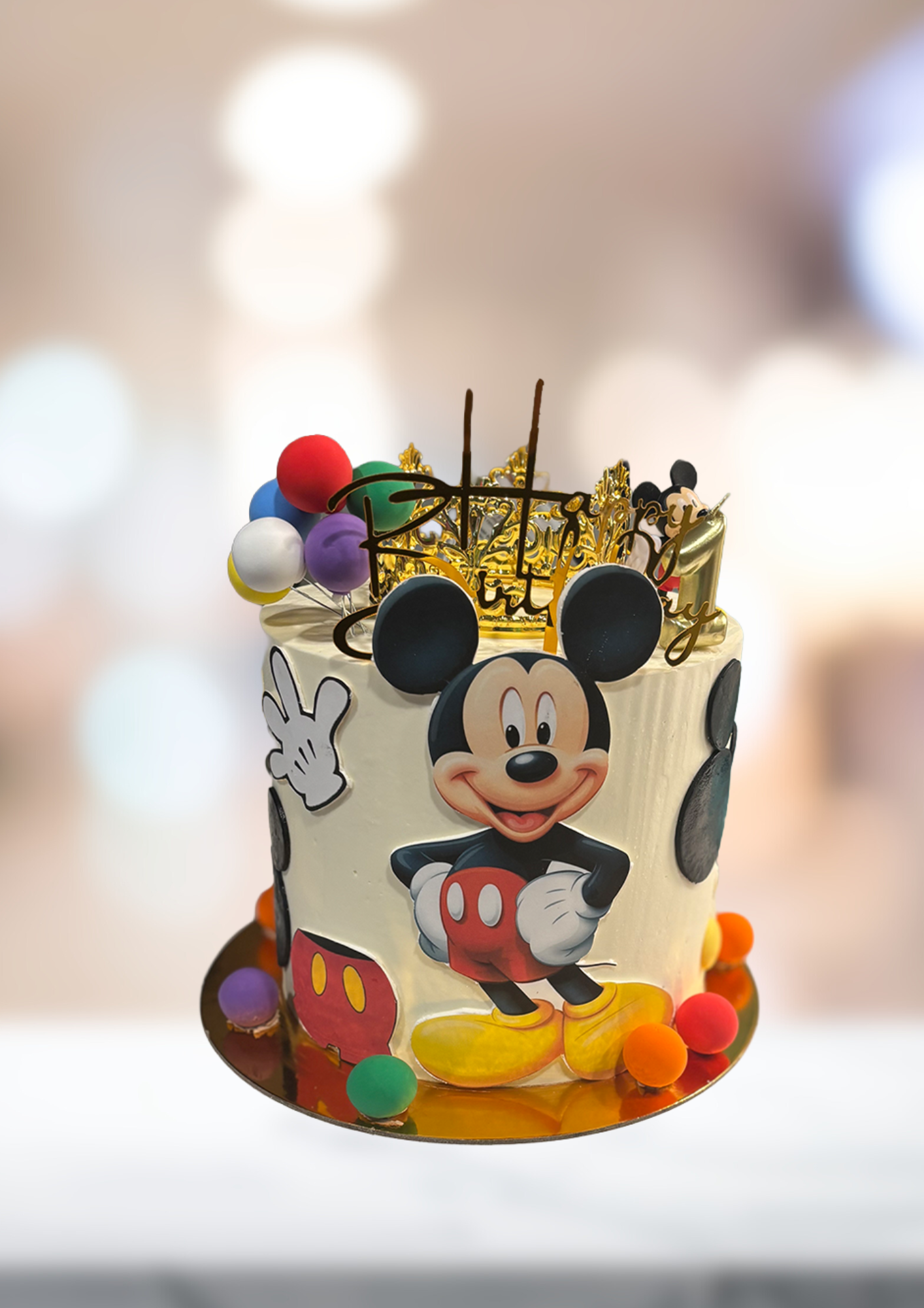 Mickey Mouse cake decorated with colorful candy and gold topper on a blurred indoor background