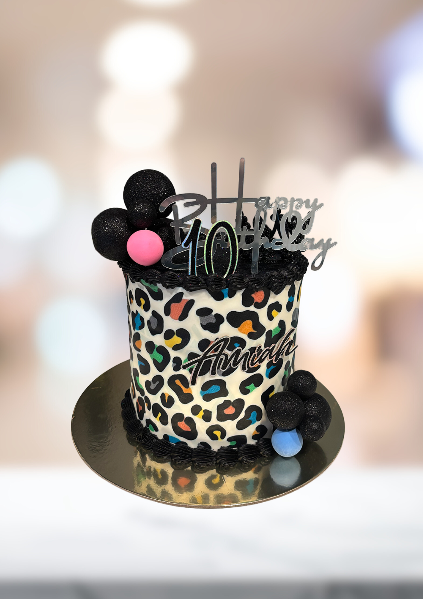 Leopard-print birthday cake with black and pink decorations on a gold cake board