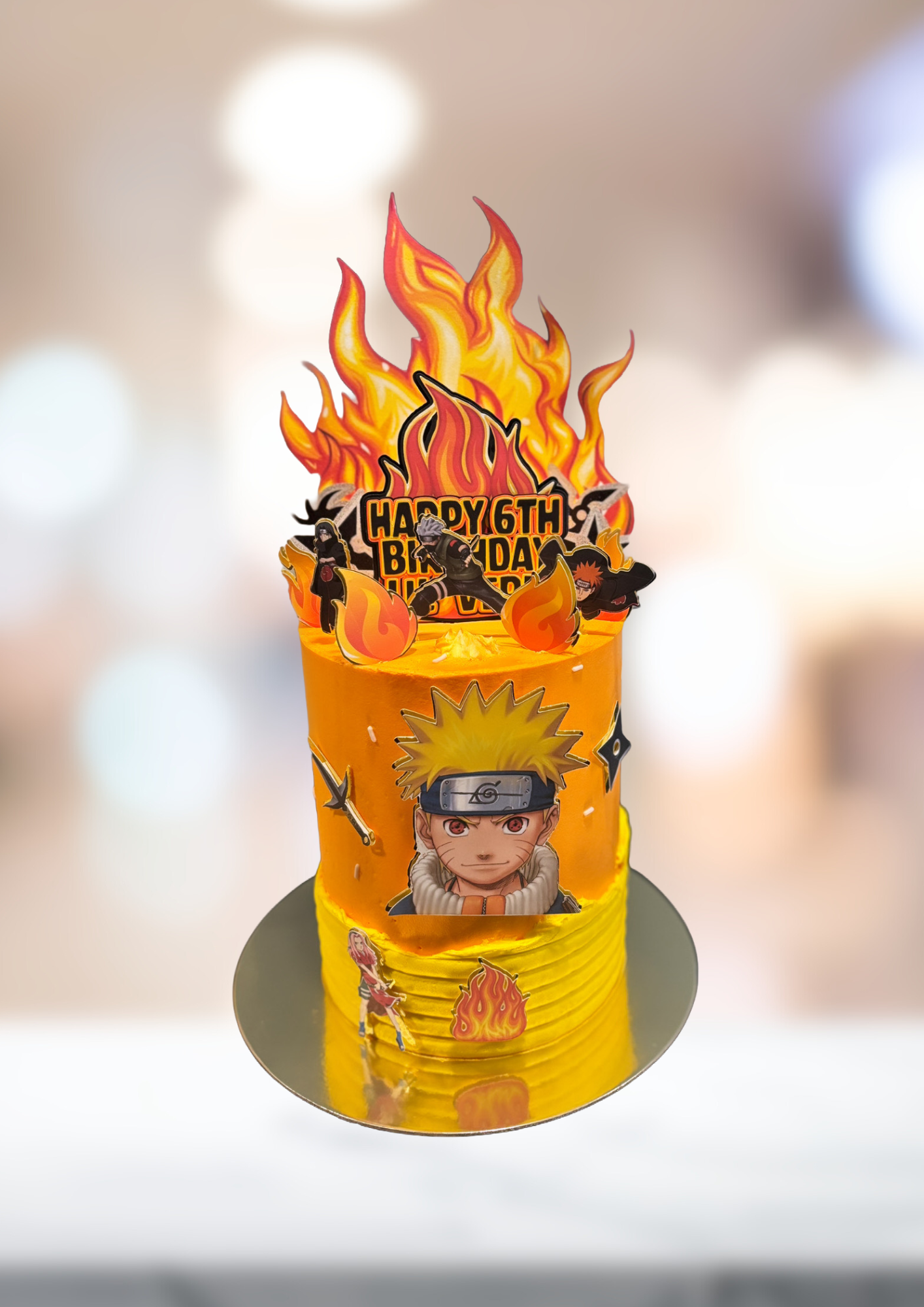 Naruto-themed yellow birthday cake with flaming topper and character image on a gold board