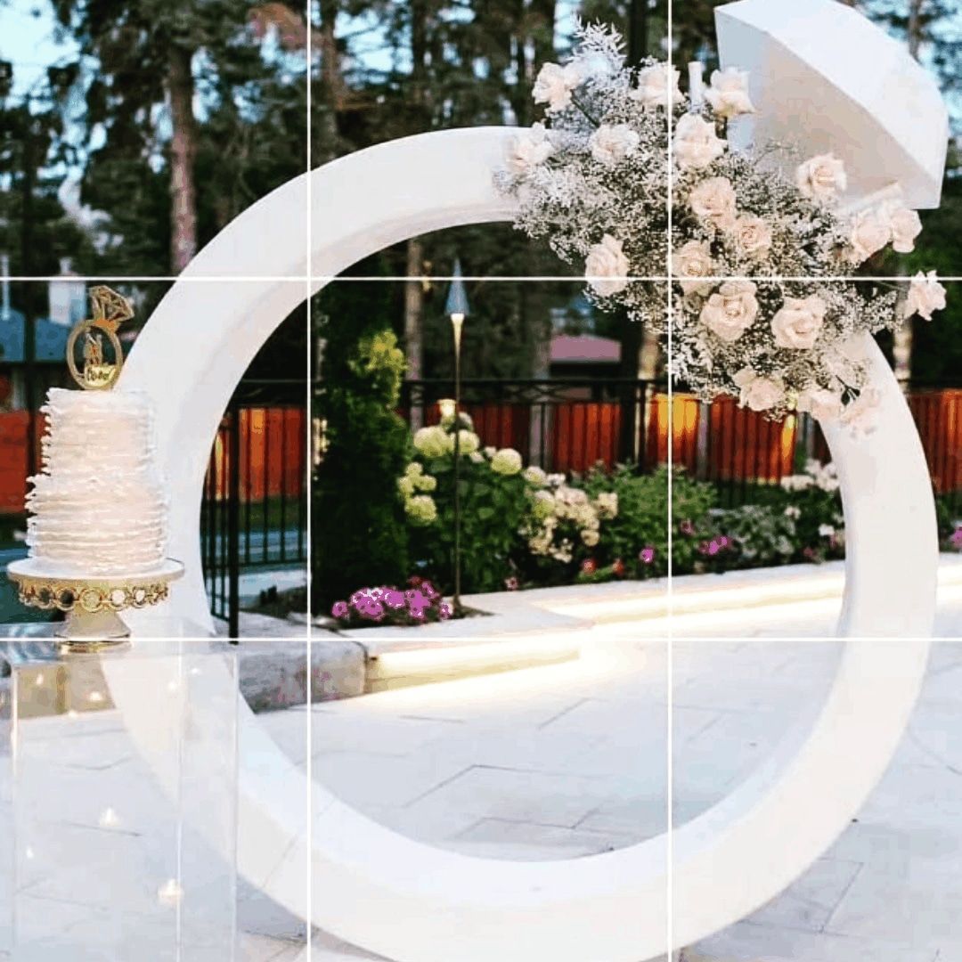 White circular wedding arch with pink and white flowers on an outdoor terrace at dusk