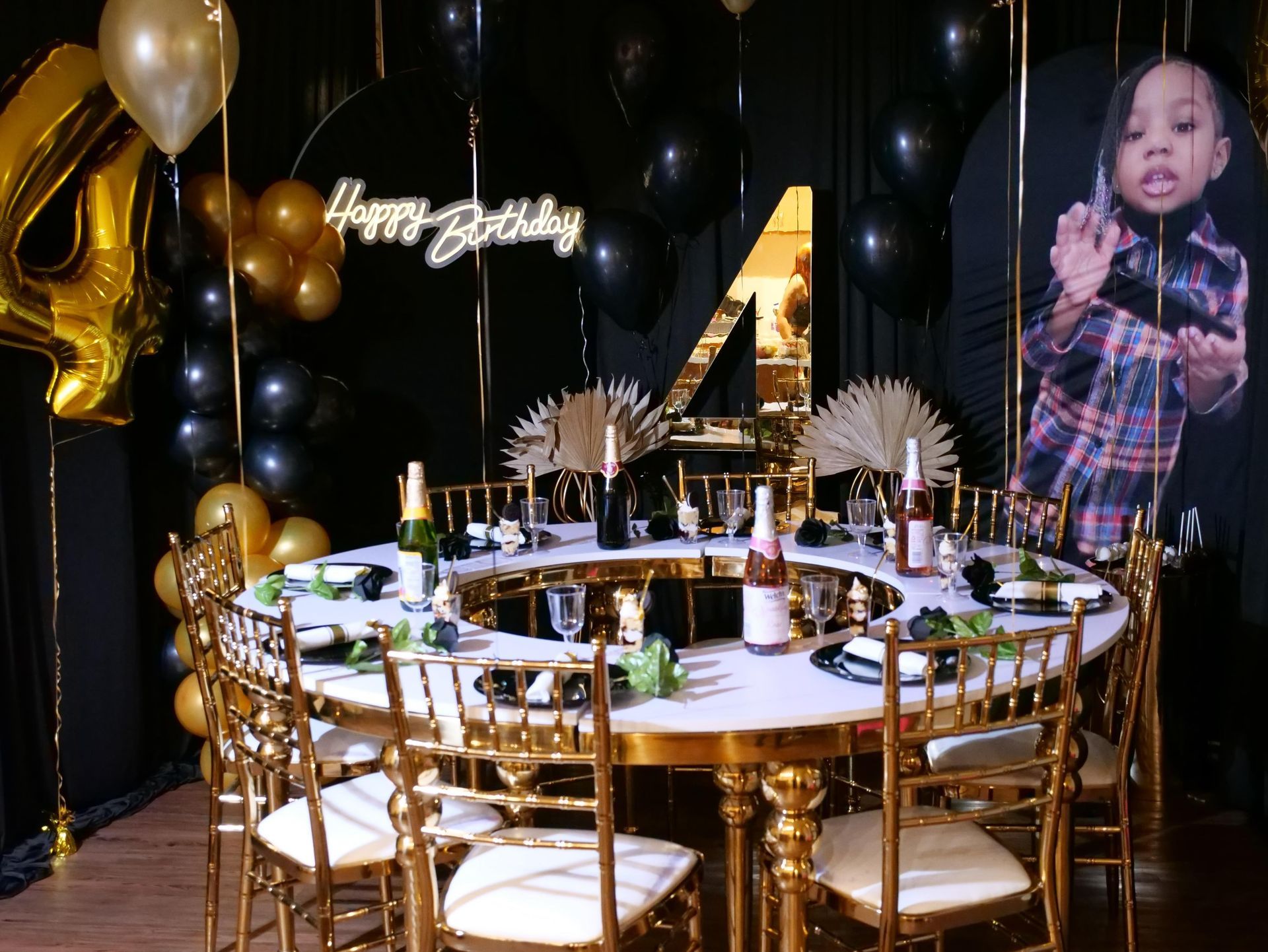 Gold-and-black birthday party setup with a round table, balloon decor, and a large number 4 backdrop