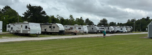 Line of white RVs parked on grass under cloudy sky, with a person walking in the foreground.