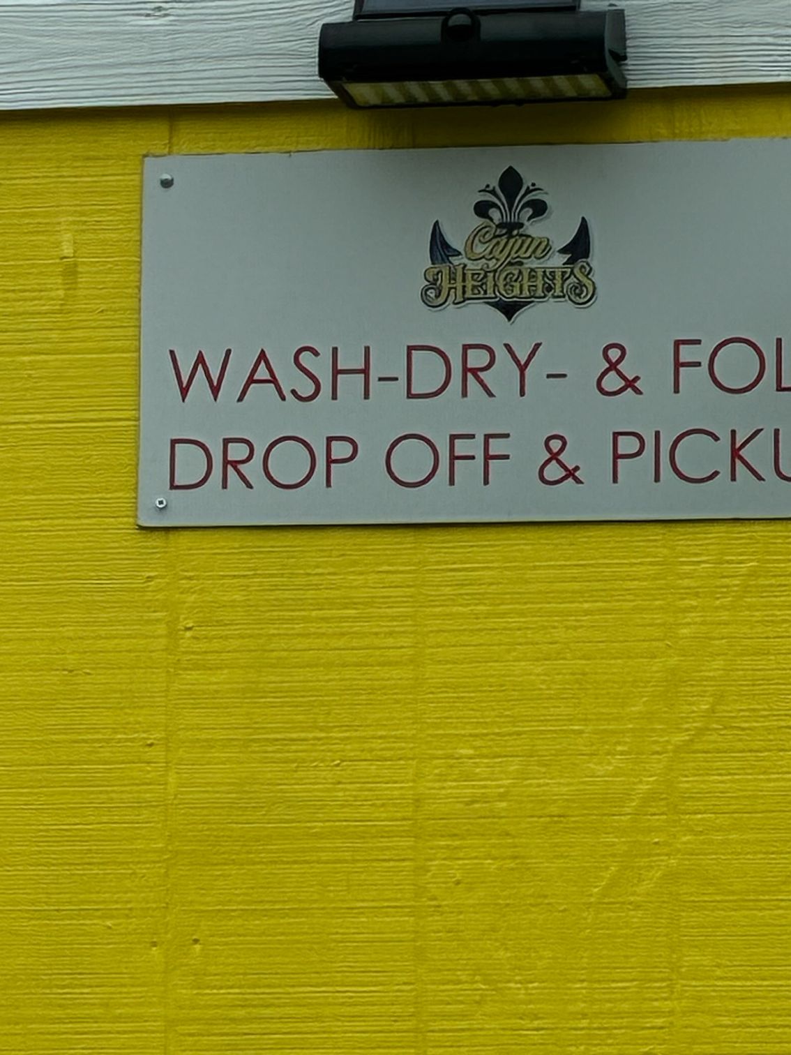 White sign on a yellow wall reads “WASH-DRY-& FOLD DROP OFF & PICKUP.”