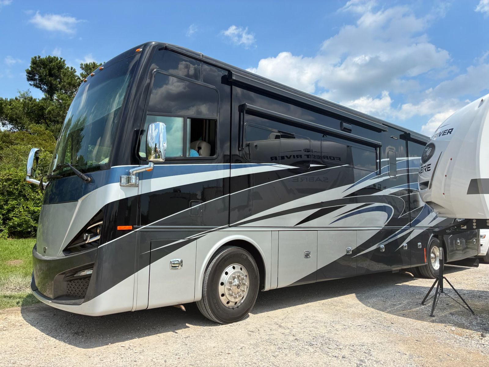 Luxury gray and black motorhome parked on a sunny roadside with blue sky above