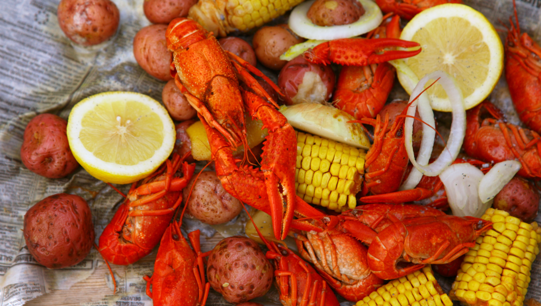 Cajun shrimp boil with corn on the cob, potatoes, lemon slices, and onion rings on a wooden table
