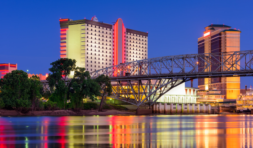City skyline at dusk with lit high-rise buildings, bridge, and colorful reflections on the water