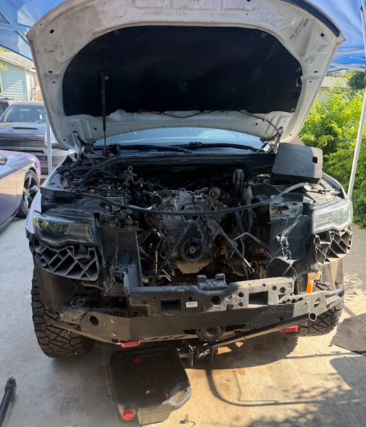 Front view of a heavily damaged black SUV with hood open and smashed front end.