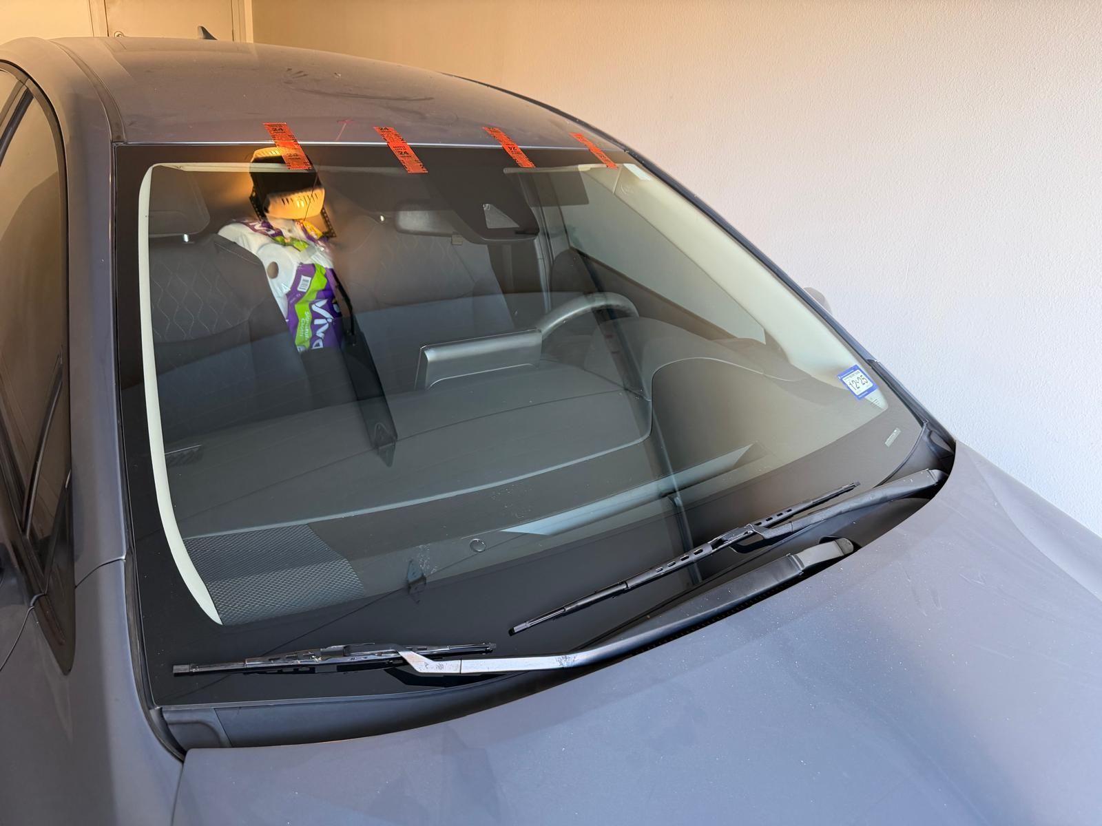 Gray car with a toy in the front, windshield wipers on.