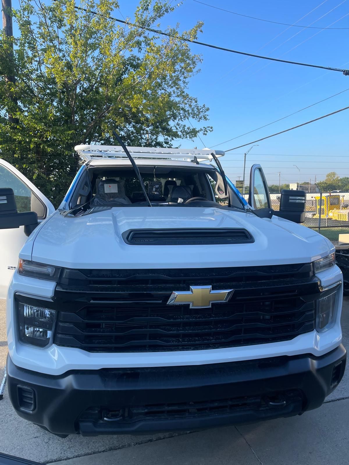 White Chevrolet truck, damaged windshield. Hood open, parked outdoors under a blue sky.