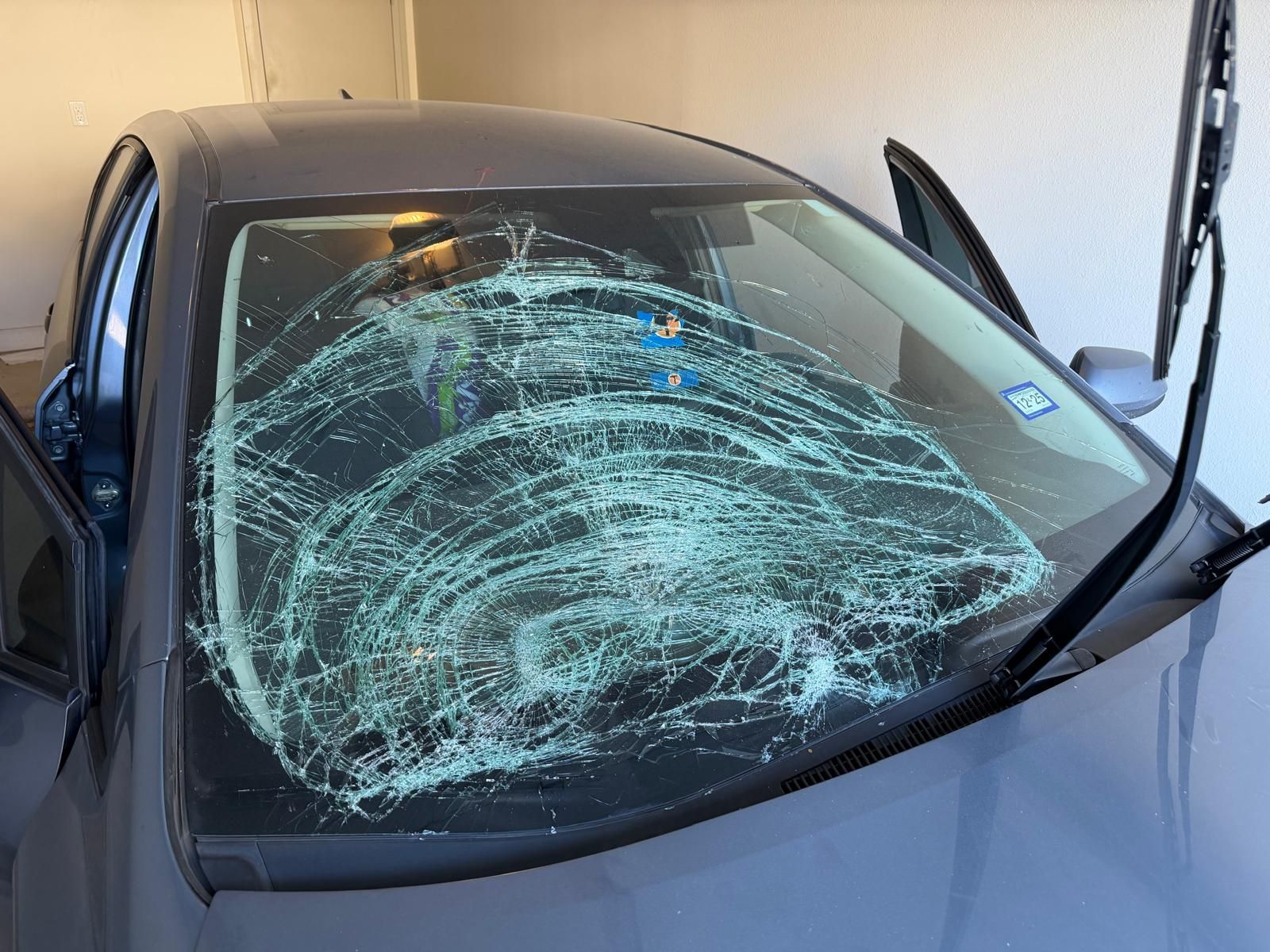 Dark gray car with shattered windshield; doors open in a garage.