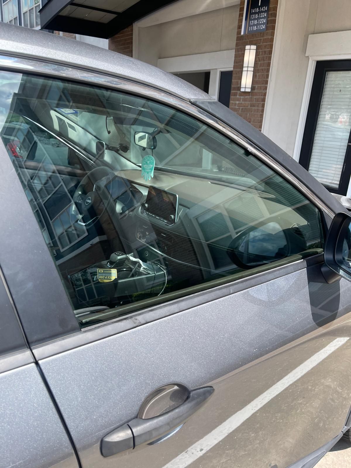 Gray car with shattered side window. Interior visible. Building in background.