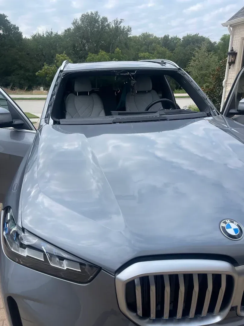 Gray BMW with a shattered windshield, parked outside. Driver's side door open, revealing the interior.
