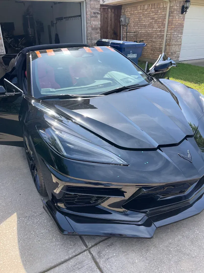 Black sports car parked in a driveway with a heavily damaged front end and crumpled hood
