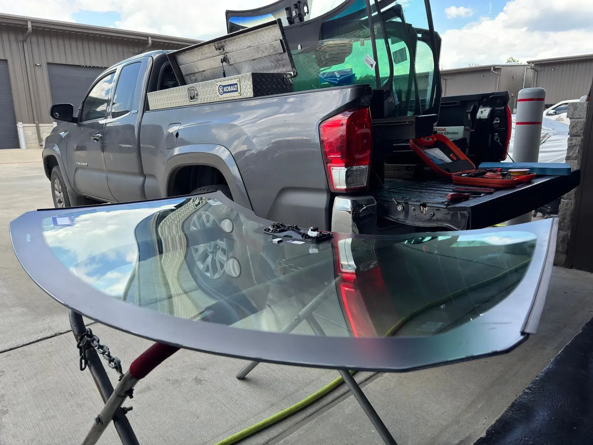 Pickup truck bed loaded with a large curved glass panel on a stand in a driveway