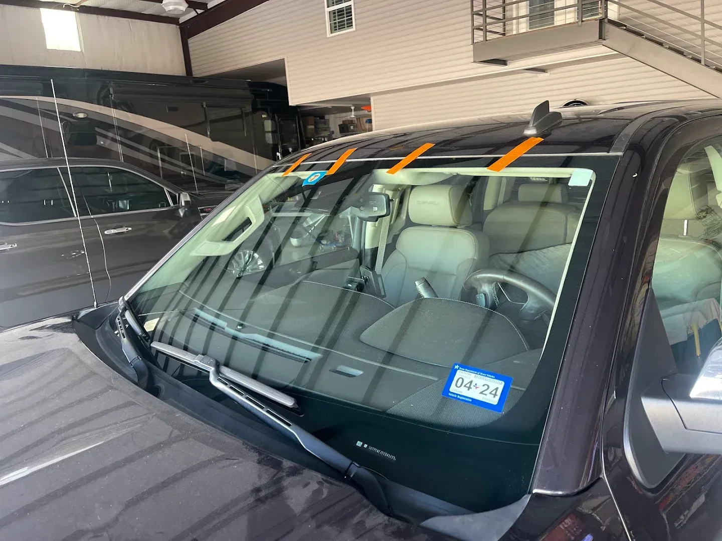A dark car with a windshield being worked on; orange tape is attached. The interior is visible.