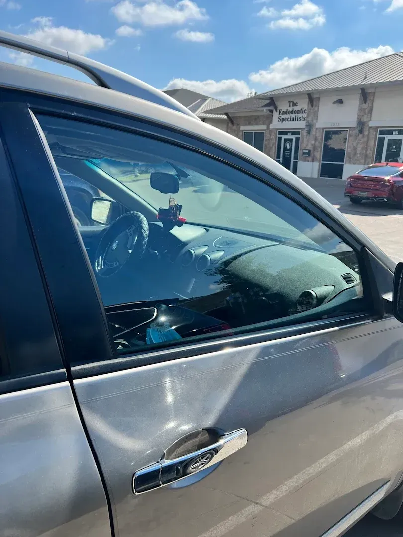 Side view of a silver car parked outside a building on a sunny day.
