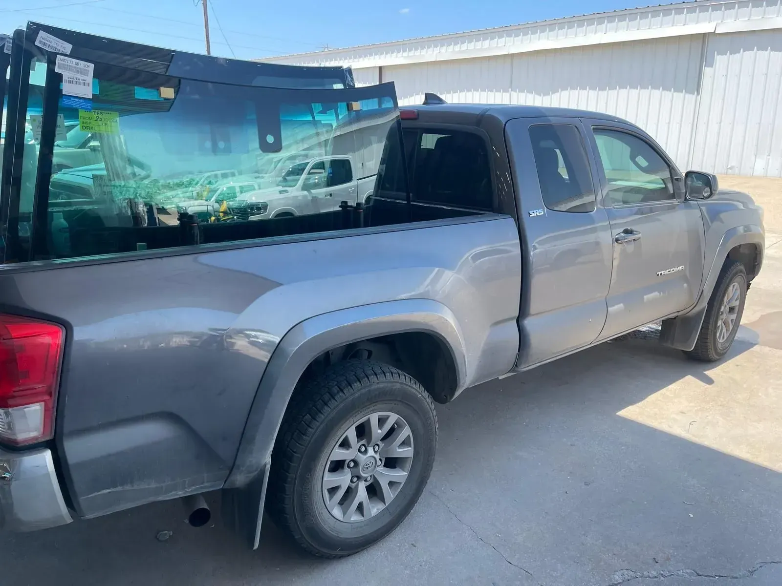 Gray pickup truck bed holding multiple glass windshields on a sunny day.