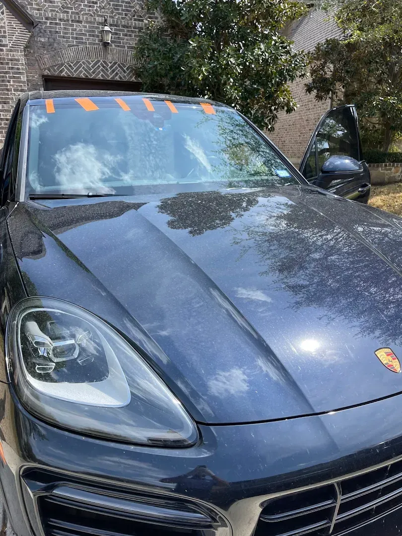 Blue Porsche SUV parked outside a brick building, orange tape on windshield, door open.