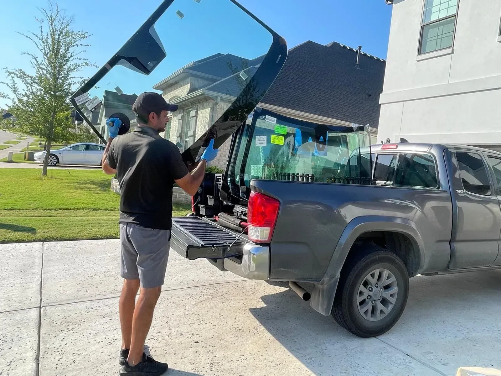 Man unloading a truck bed with a windshield in a residential driveway.