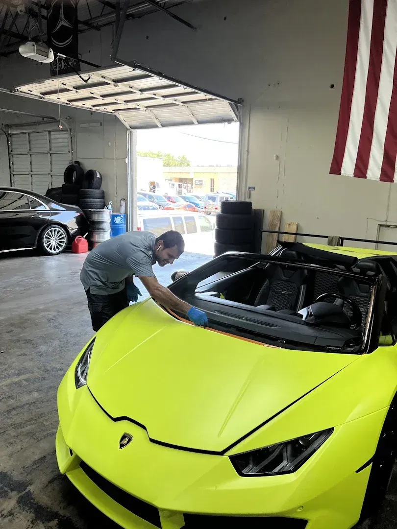 Mechanic leaning over a neon yellow sports car in a garage, with an American flag hanging nearby.