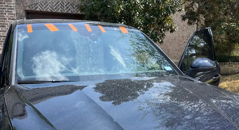Black car with wet windshield and open driver's side door, orange tape across the top.