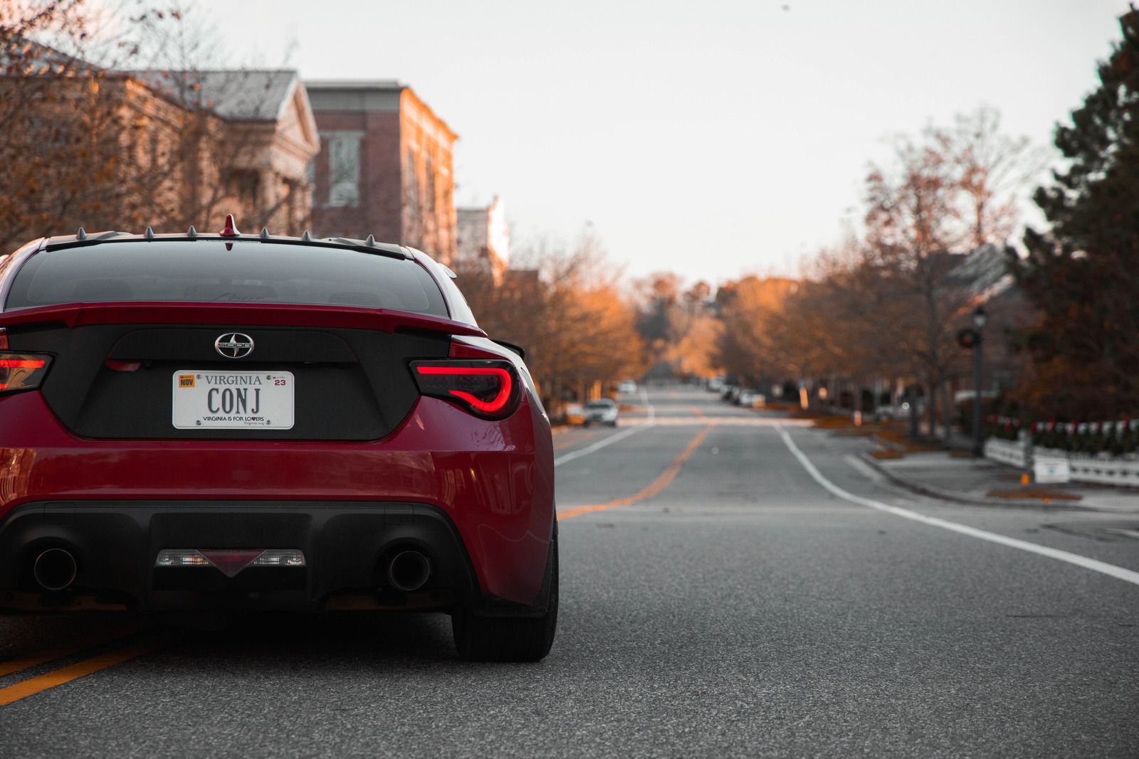 Red sports car parked on a road in a small town, autumn trees, and buildings in the background.