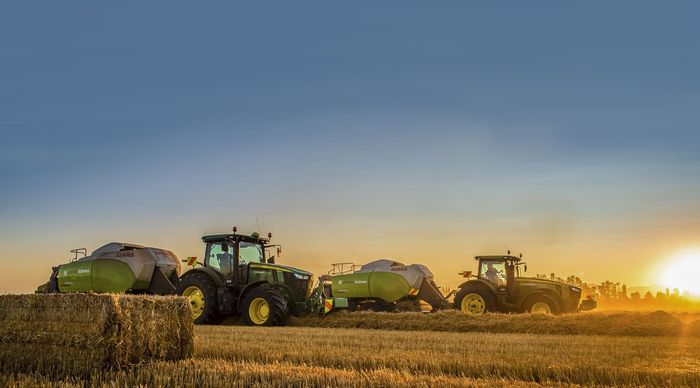 Three john deere tractors are working in a field at sunset