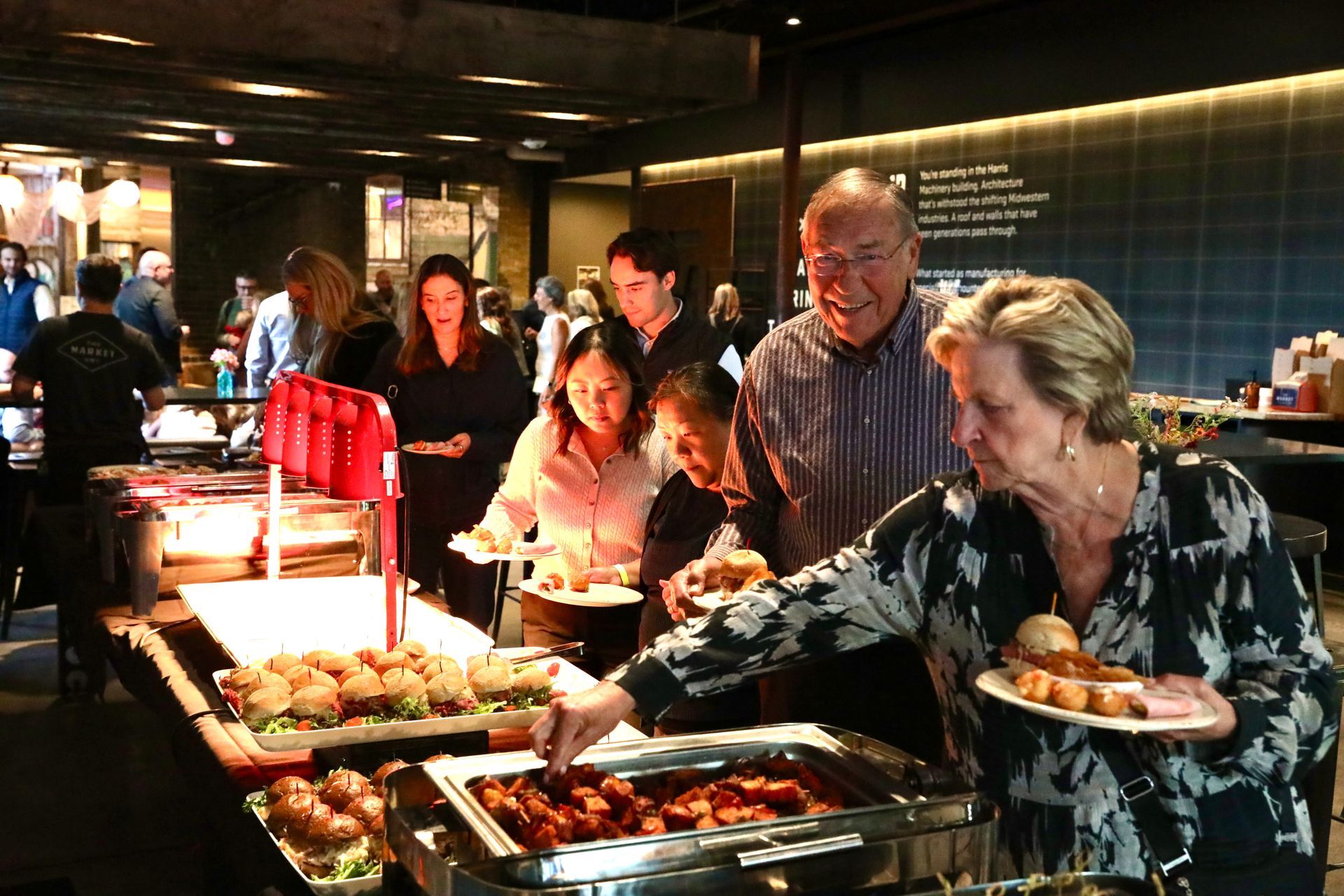 People at a buffet, selecting food. Indoors, warm lighting.