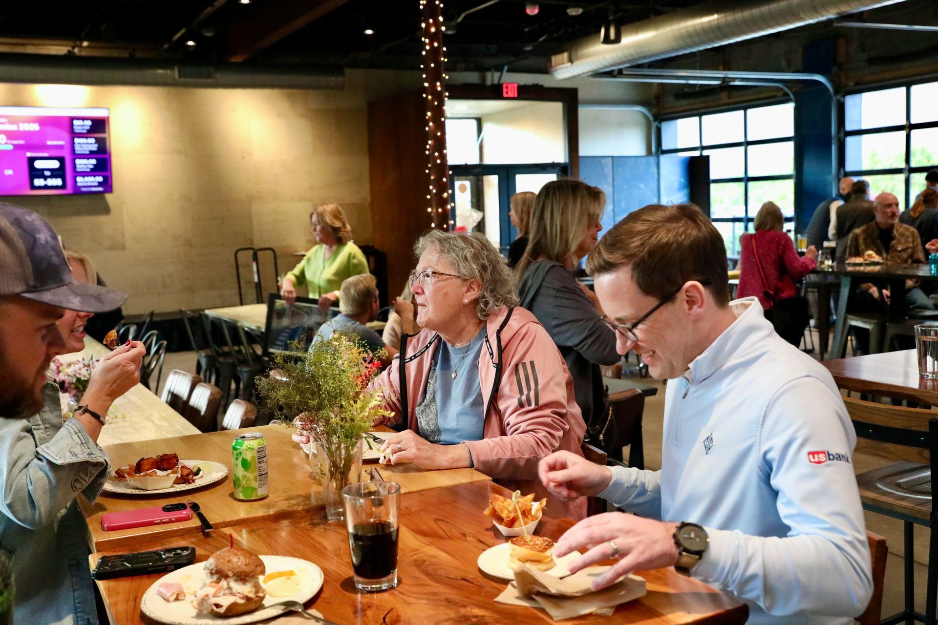 People eating and conversing at a restaurant. A man in a light blue shirt eats a sandwich.