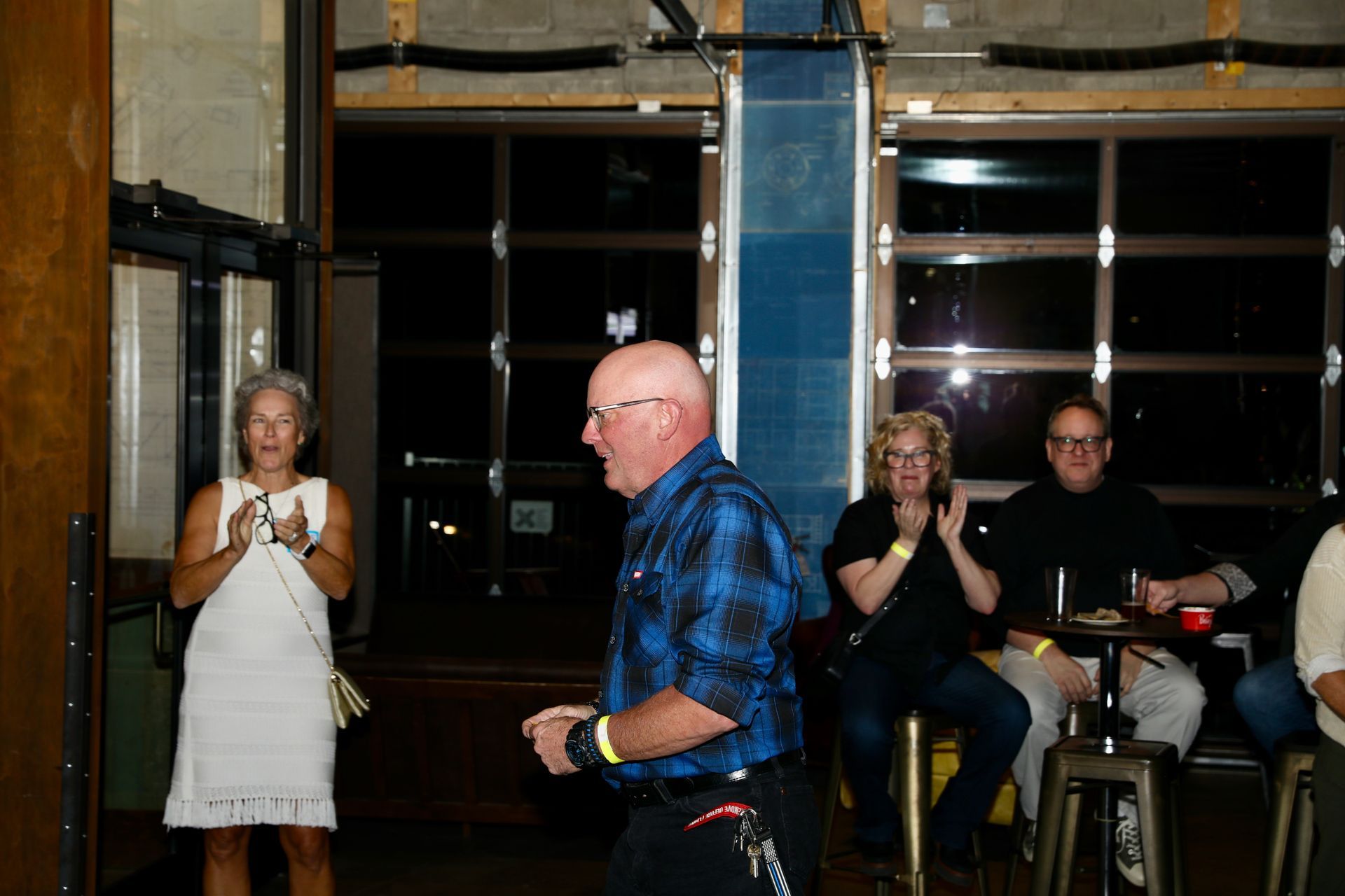 Man in blue shirt walks, applauded by people seated and standing in a venue.