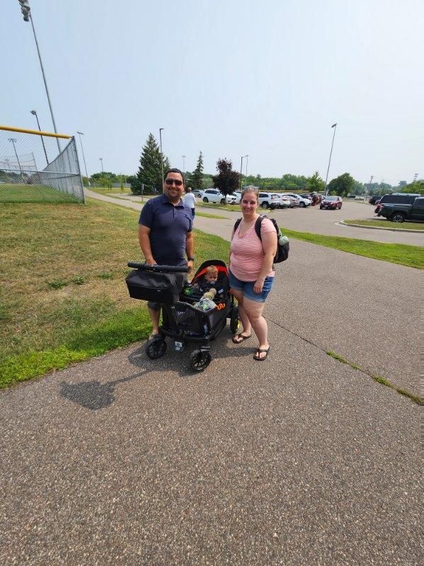 Family with a stroller on a paved path near a park. The child is in the stroller. Sunny day.