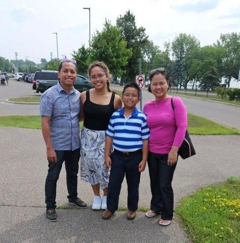 Family of four smiles for the camera, posing outdoors on a sunny day.