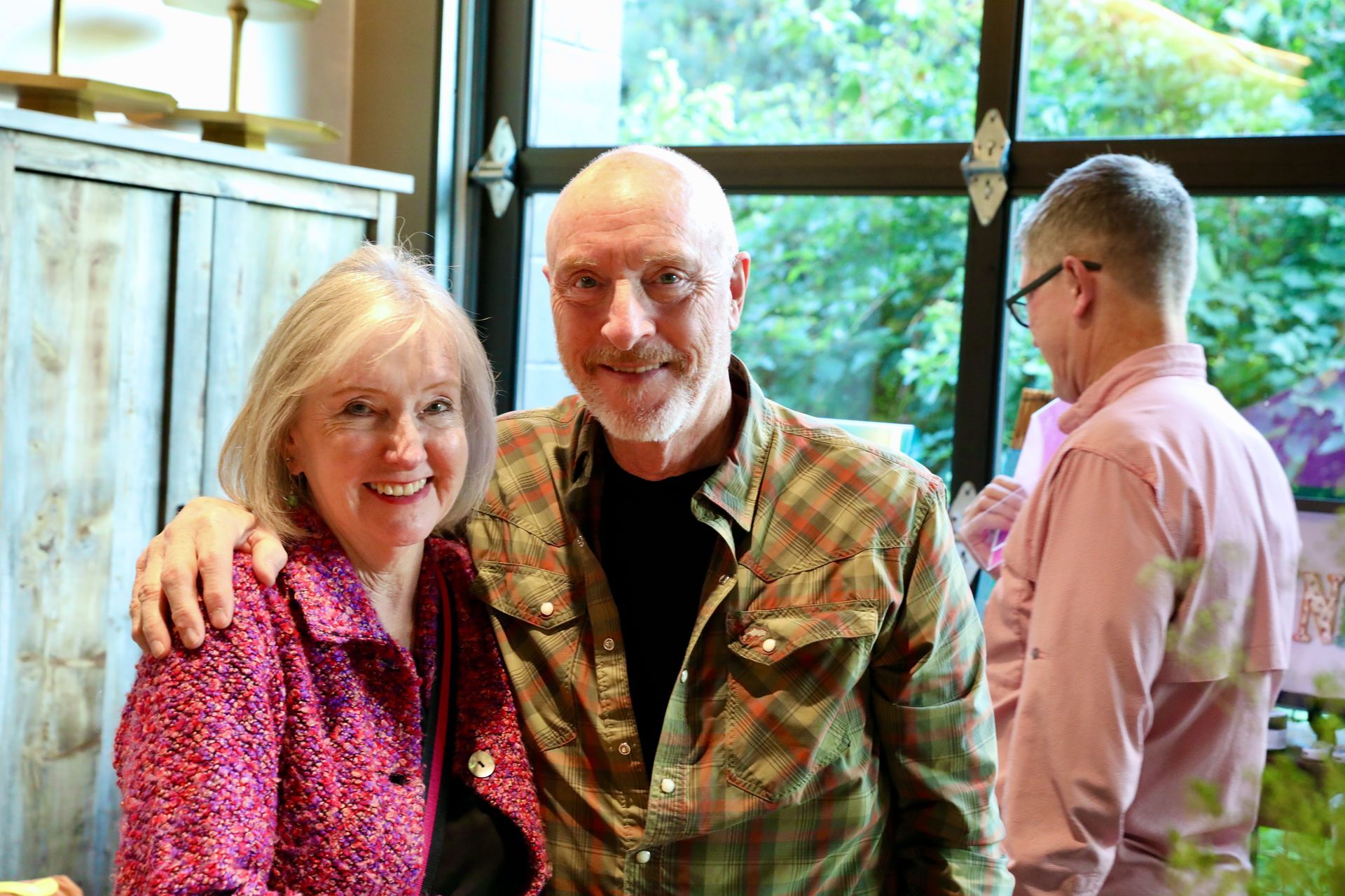 Woman and man smile together indoors; man's arm around her shoulder. Another man stands behind them.