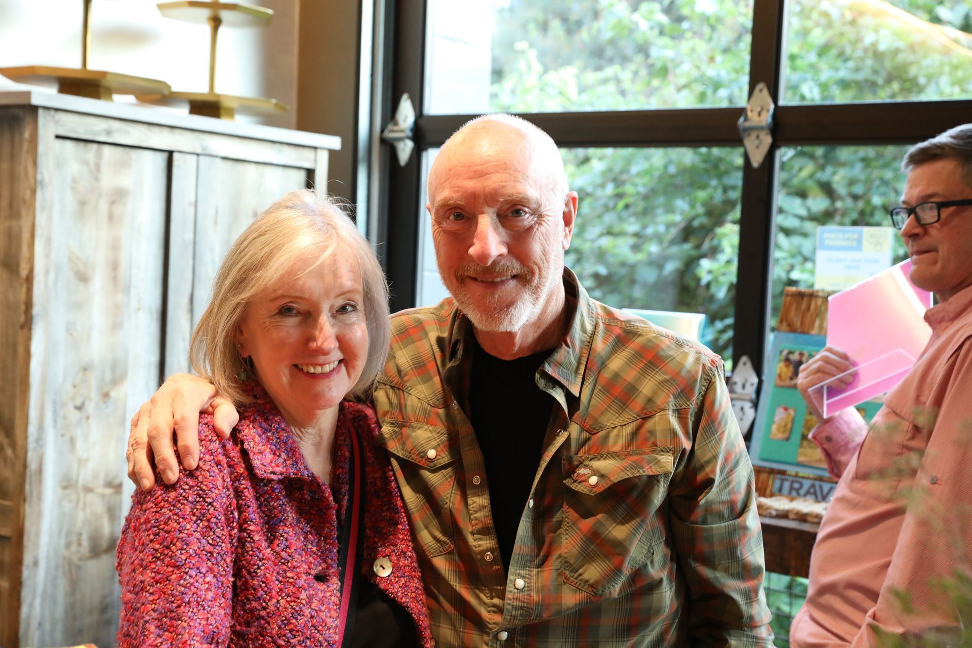 Smiling people posing indoors; woman in red, man in plaid shirt, other man partially visible.