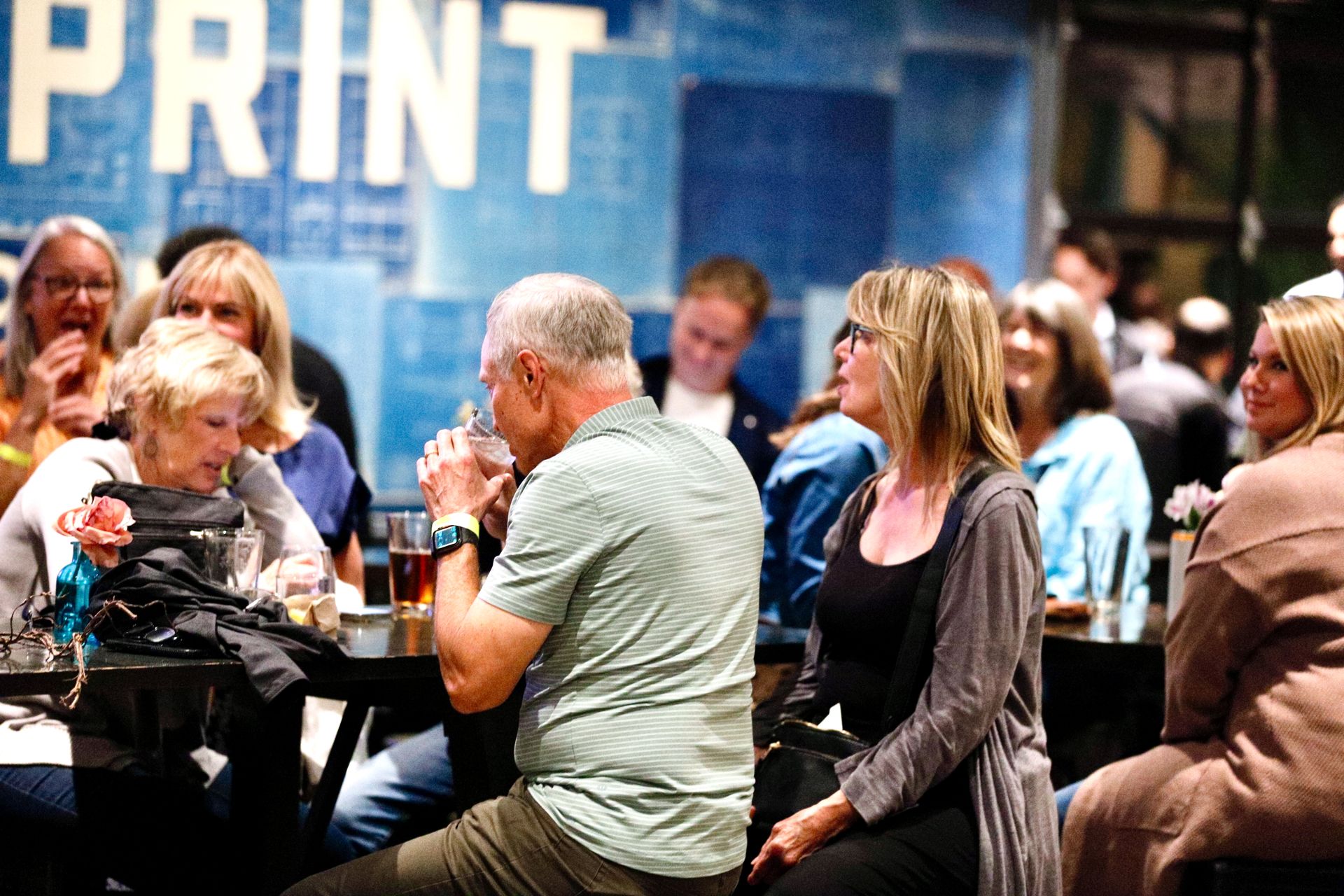 People at tables in a blue-lit space, some drinking. 
