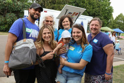 Group of people smiling, posing in front of a service vehicle at an outdoor event.