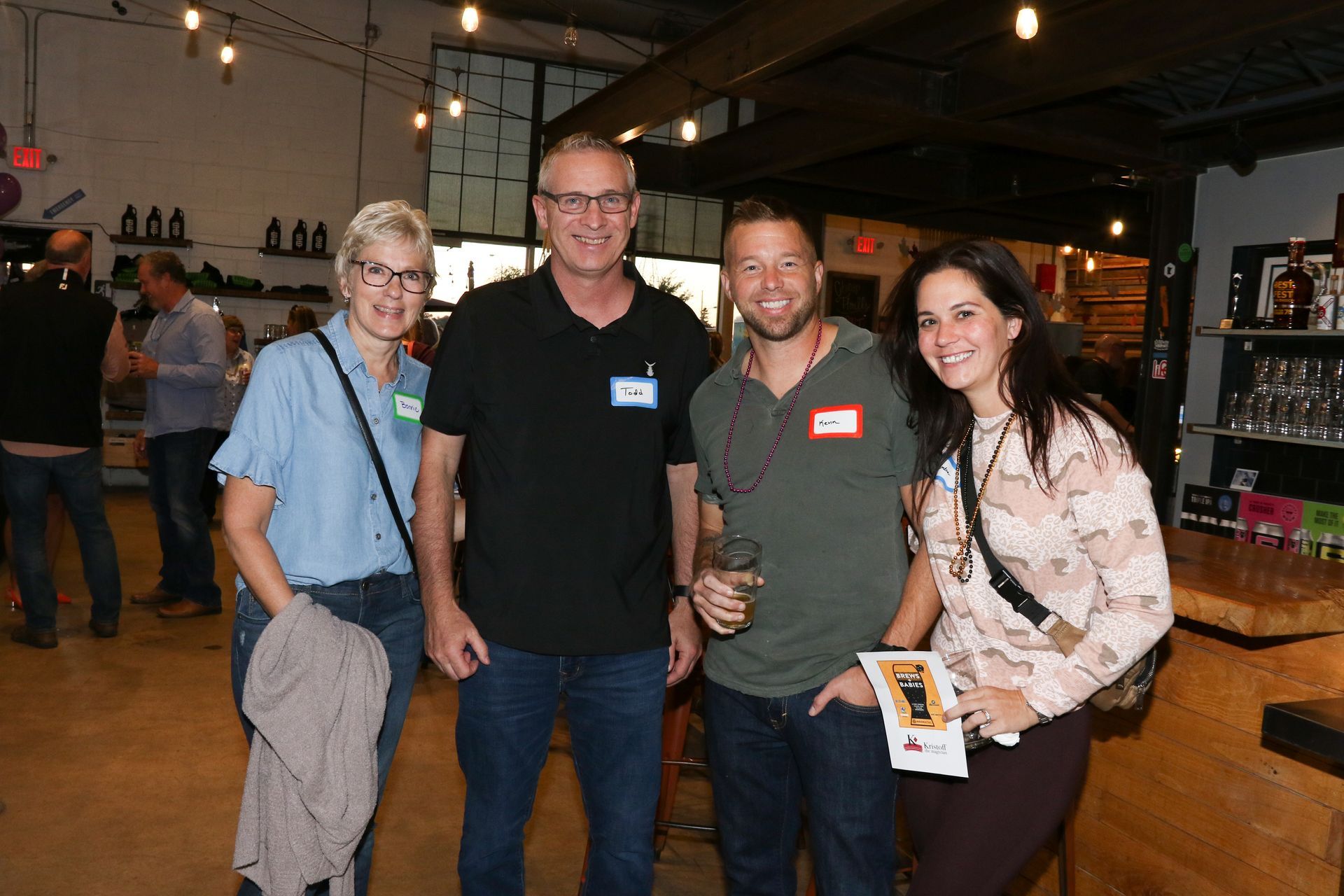 Four people smiling, posing together inside a brewery.