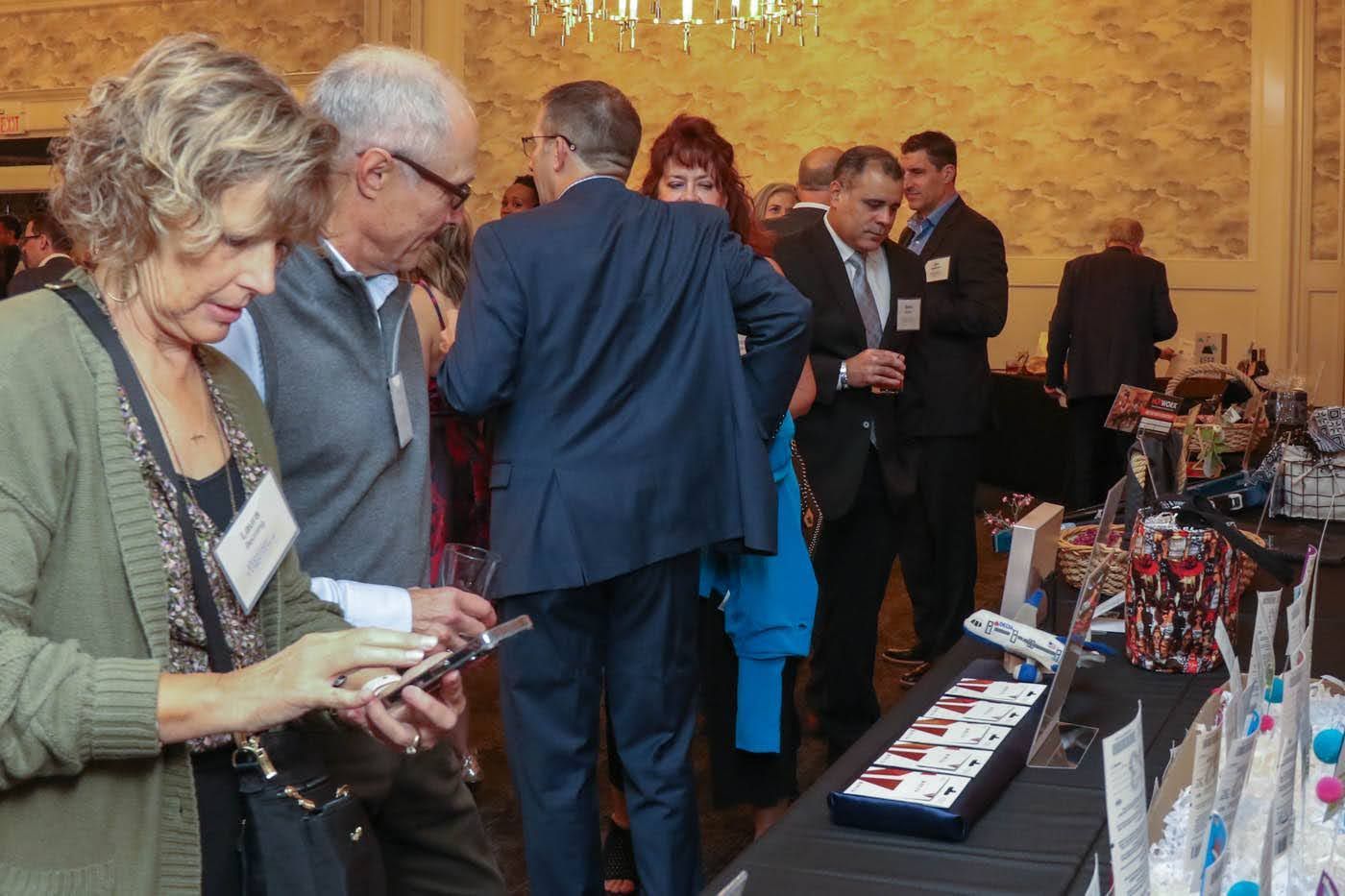 People at an event looking at items on display; a woman checks her phone.
