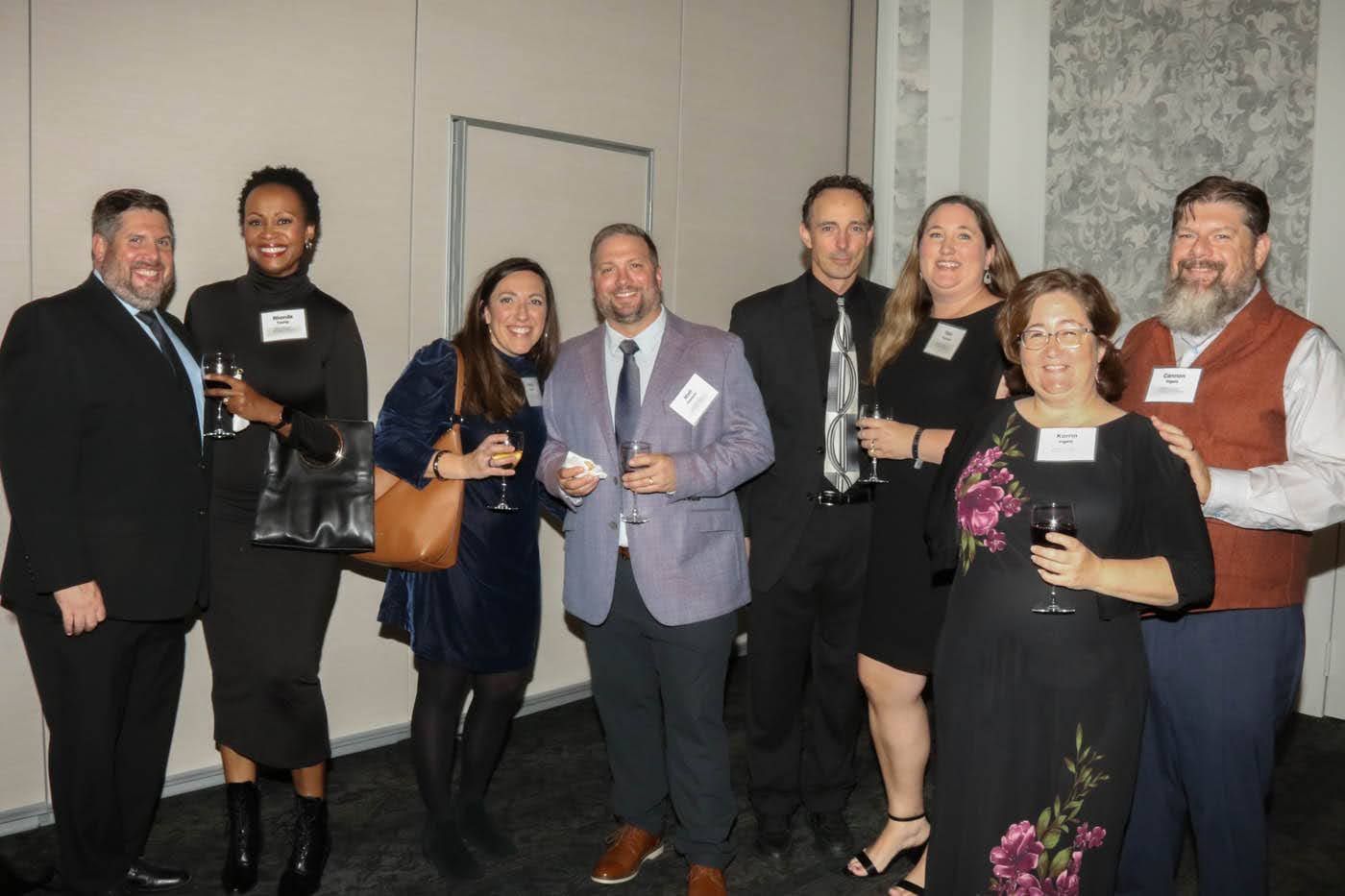 Group of nine people in formal attire pose for a photo at an event.