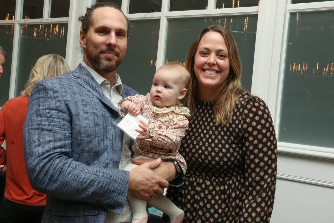 Man holding baby, woman smiling, all near a window, festive setting.