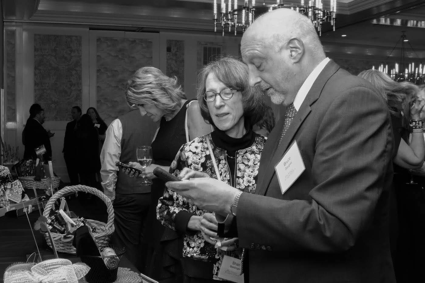 People examining items at an event with baskets. Man in suit points at something. Others look on in a room.