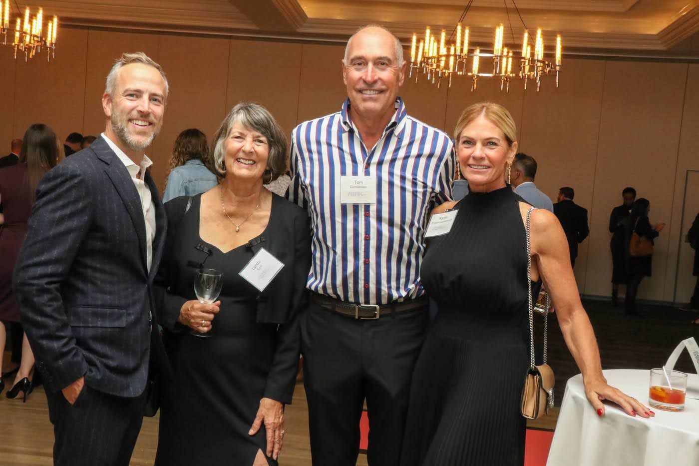 Four people posing for a photo at a reception; two women and two men smiling, in formal attire.