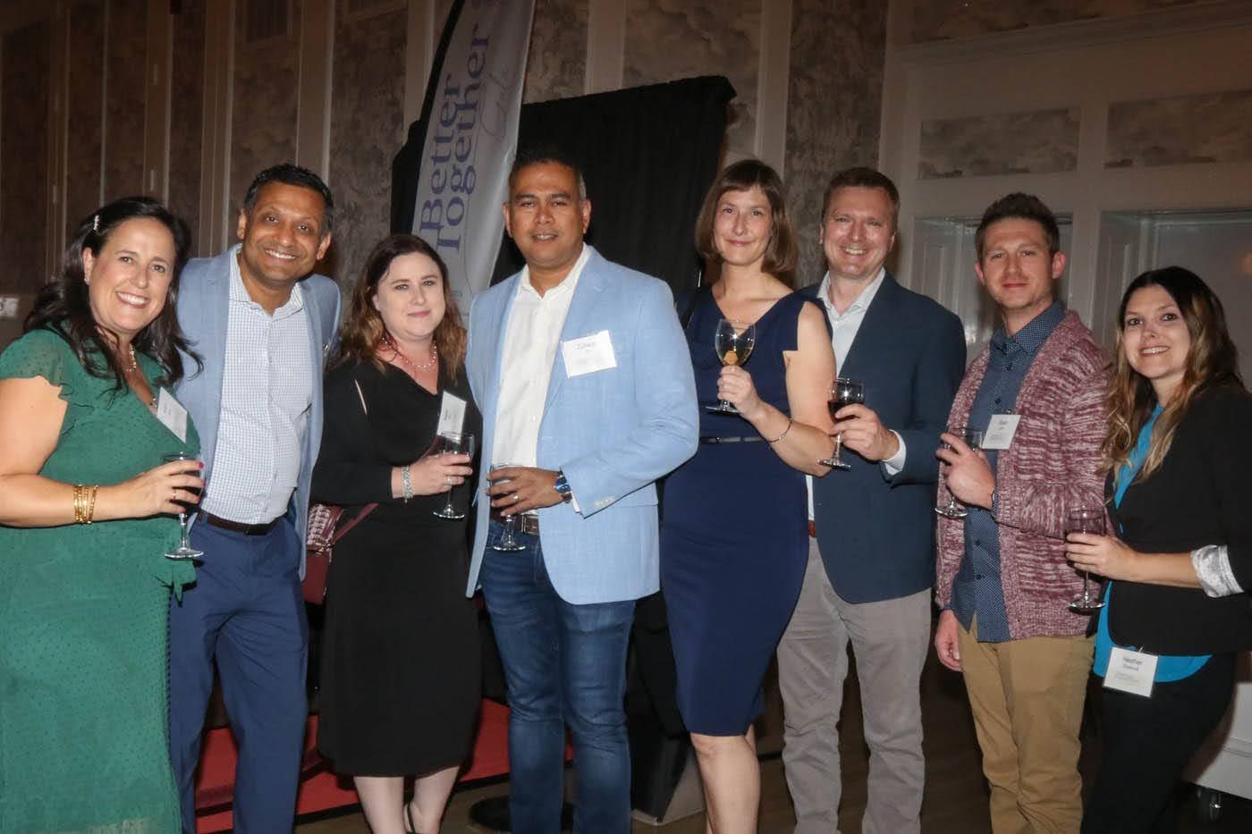 Group of people at an event, some holding drinks, in a well-lit indoor space.