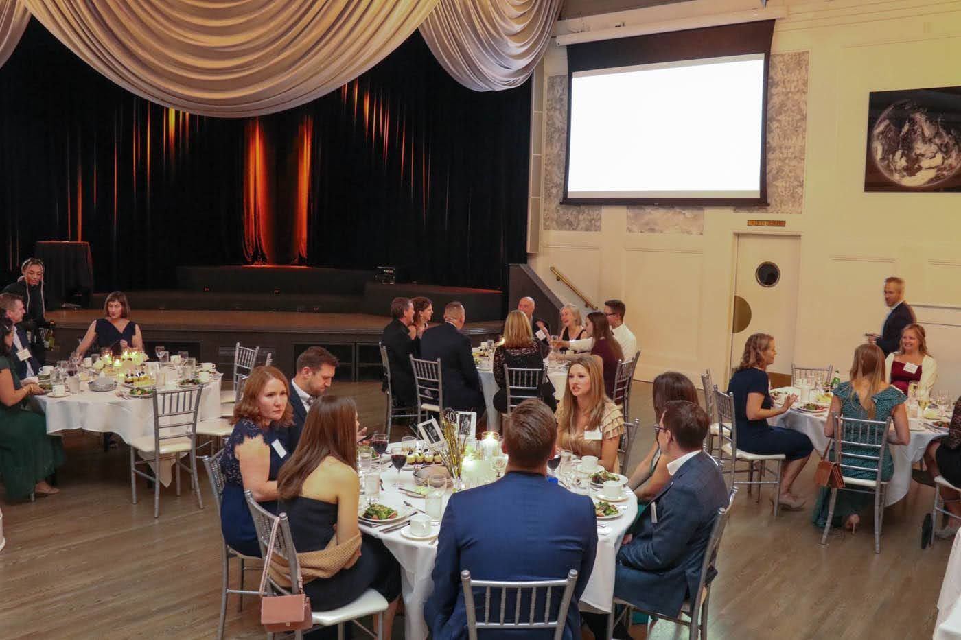 Guests seated at round tables in a decorated event space with a stage.
