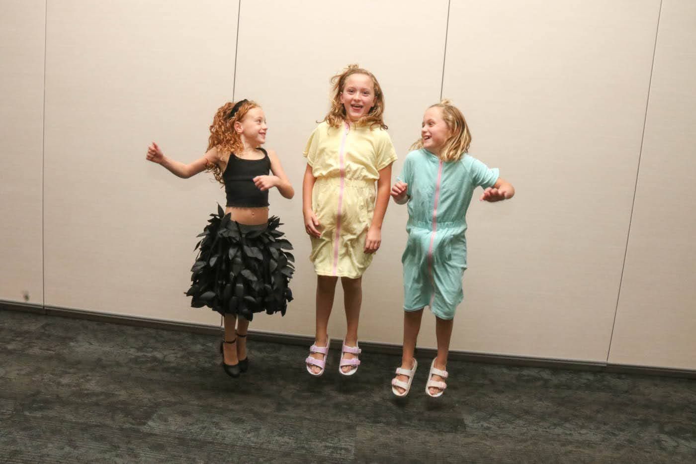 Three girls jumping and smiling in front of a neutral wall.