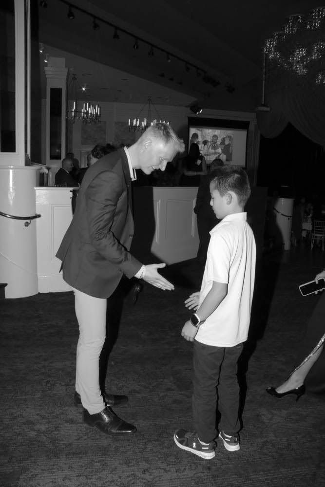 Man in blazer shaking hands with boy in white shirt. Inside.