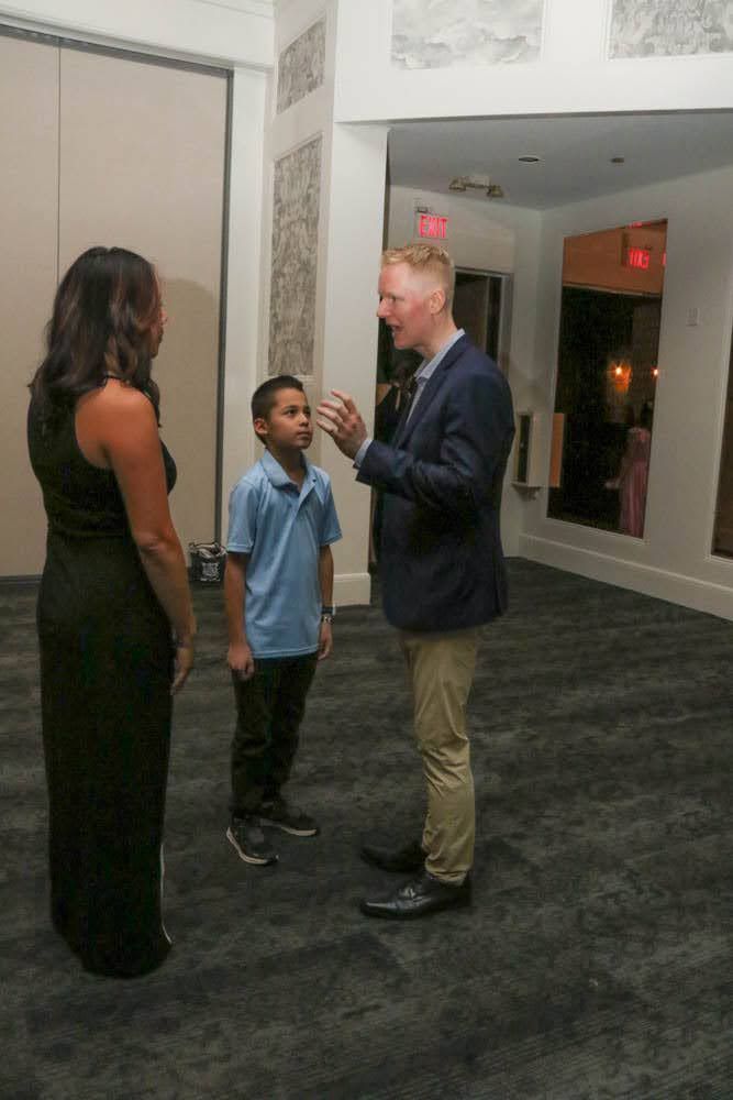 Man in blazer talks to a boy and a woman in a formal setting.
