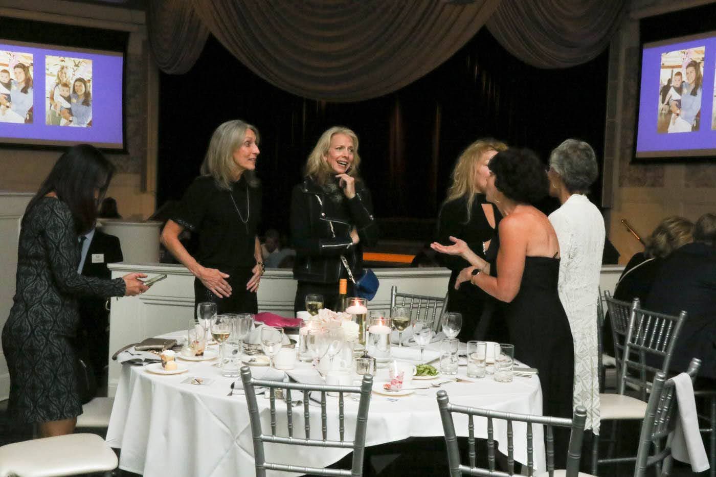 People at a formal event, gathered near a round table, talking.