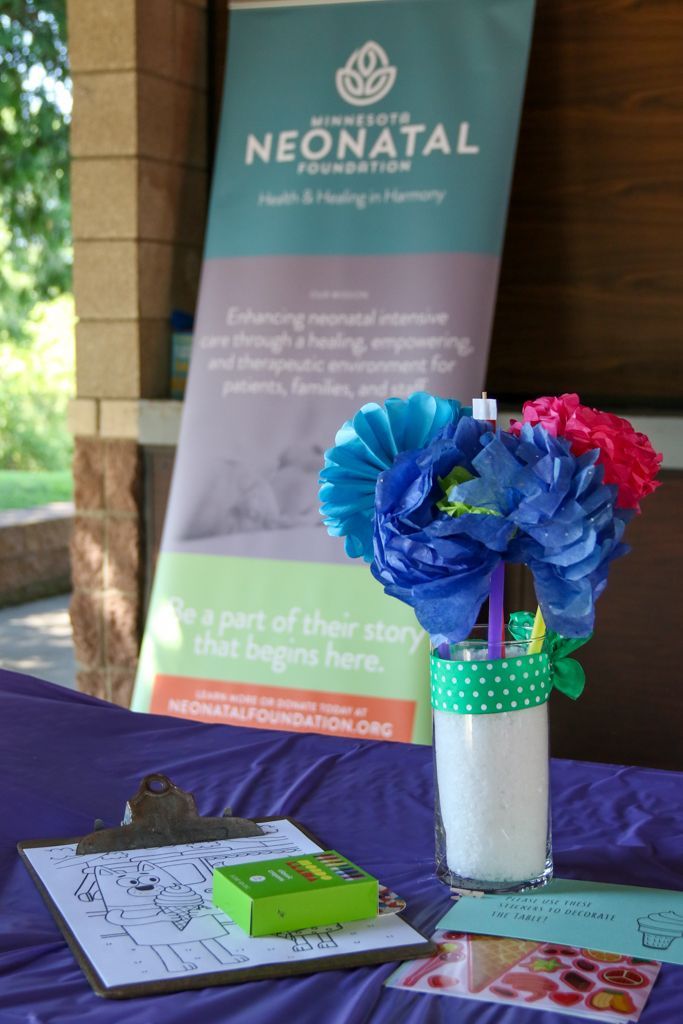 Table with decorations and banner for a neonatal health event. Blue and pink paper flowers in a vase, clipboard, and green box.