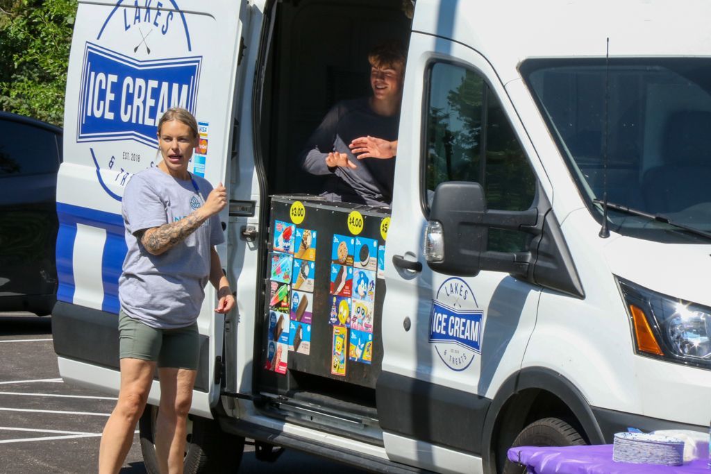 Ice cream truck with two people: one outside gesturing, one inside. White van with ice cream signage.